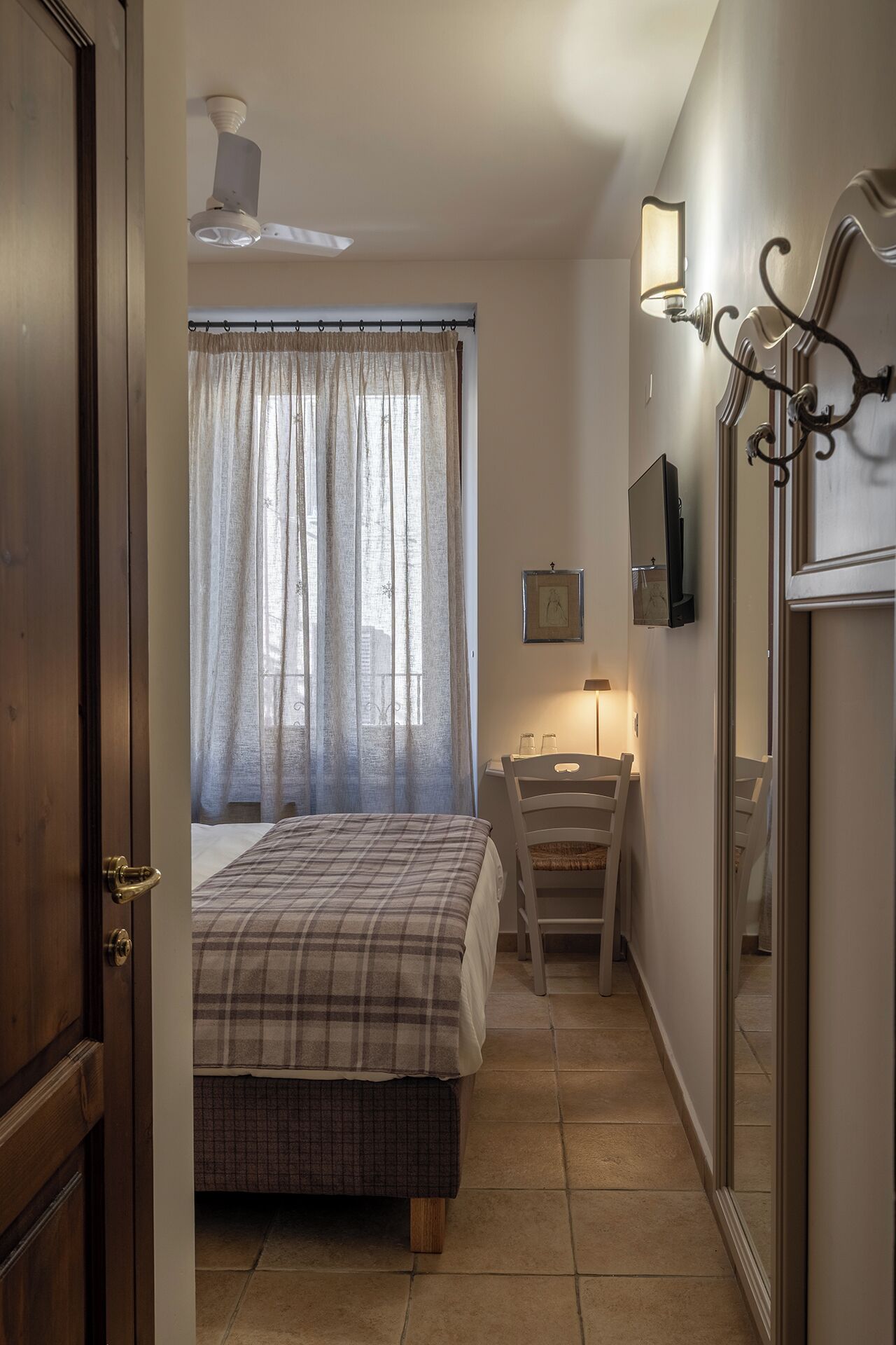 Een slaapkamer met een bed, een stoel, een bureau, een lamp en een spiegel.
