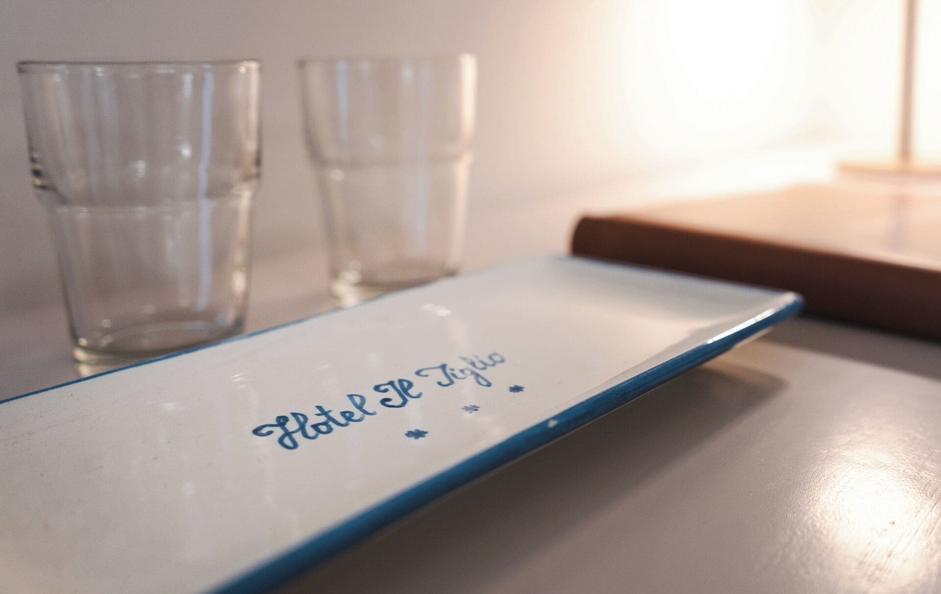 Un plato blanco con la leyenda 'Hotel de Tiglio', colocado sobre una mesa con dos vasos vacíos a su lado.