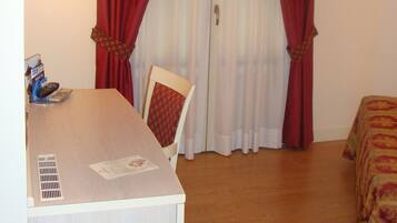 A hotel room with a bed, a desk with a chair, a television, and a window with red curtains.