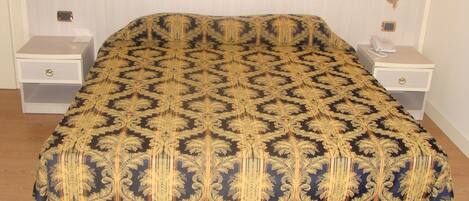 A bed with a patterned bedspread, two bedside tables with lamps, and a nightstand with a phone.