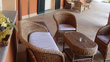 Un espacio de estar al aire libre con techo, muebles de mimbre y una planta en maceta.