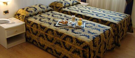 Una habitación de hotel con dos camas, una mesita de noche con lámpara y una bandeja con cosas para el desayuno.