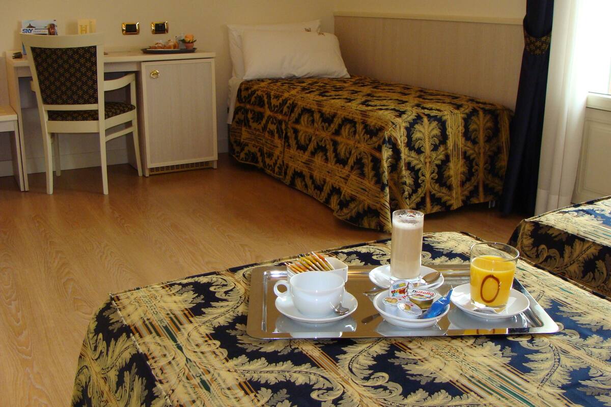 Una habitació d'hotel amb un llit, una taula de treball i una cadira. Hi ha un safata amb articles per l'esmorzar, incloent-hi una tassa, un got de suc i un bol de cereals.