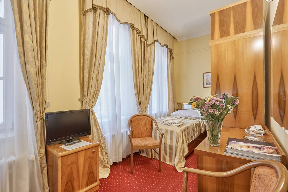 Habitación de hotel con cama, escritorio, computadora, silla, televisor y un florero con flores.