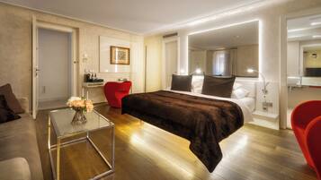 Une chambre d’hôtel moderne avec un grand lit, une table basse en verre, un fauteuil rouge et une petite table sur laquelle est posé un vase de fleurs.