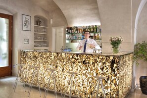 Een bar met een uniek getextureerd aanrecht, barstoelen en diverse flessen op planken.