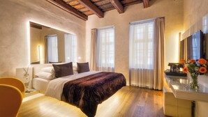 A modern bedroom with a large bed, a bedside table, a mirror, and a desk with a vase of flowers. - Hotel Three Storks (Prague)
