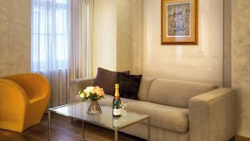 Un salon avec un canapé beige, une table basse en verre ornée de fleurs, un fauteuil jaune et un plafond décoré de motifs floraux.