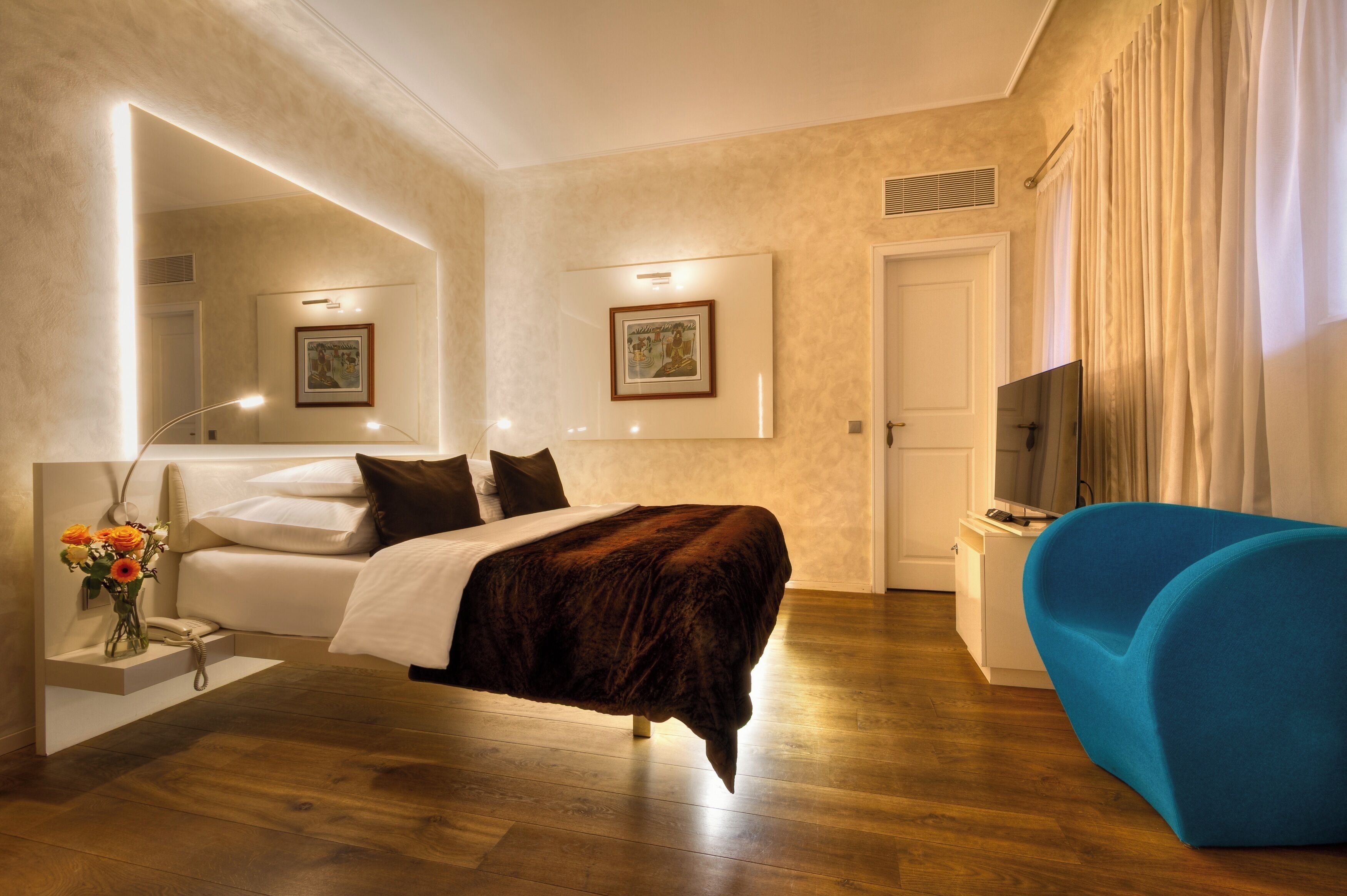 Habitación de hotel moderna con una cama grande, un sofá azul, un televisor de pantalla plana y un espejo.