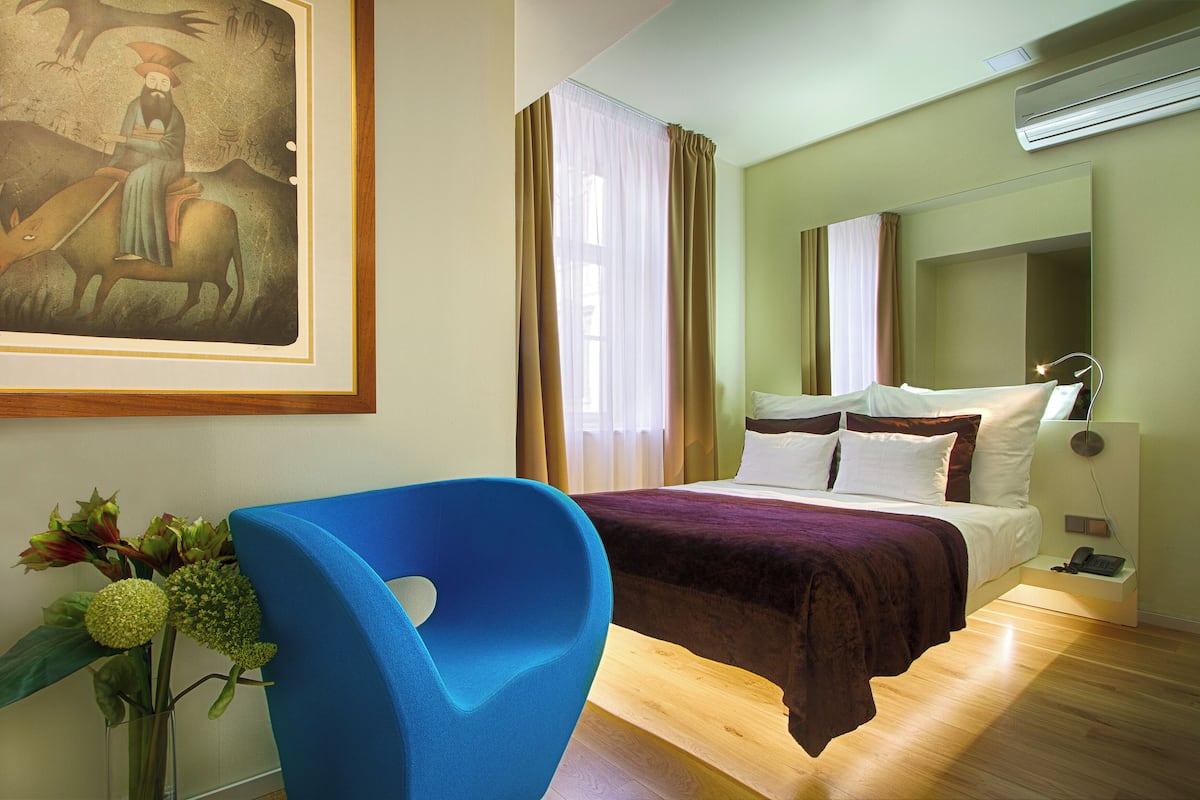 Une chambre d’hôtel avec un grand lit, une chaise bleue, un tableau au mur et un vase rempli de fleurs.