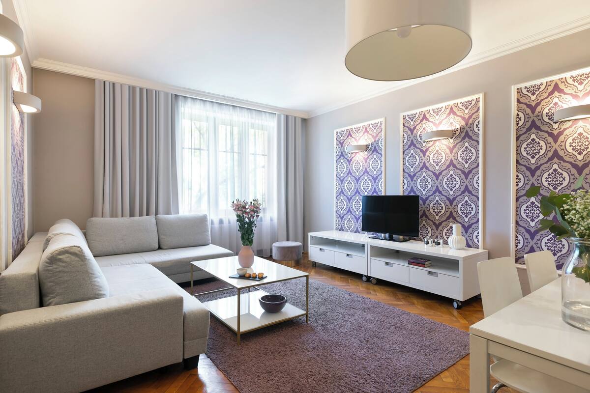 En moderne stue med en grå sofa, et sofabord, et tv på et hvidt skærm og tapet med mønster.