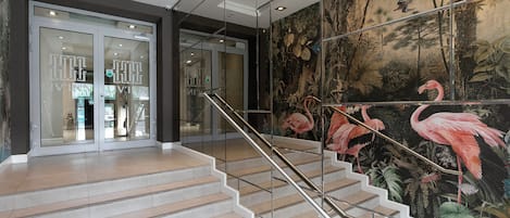 Una escalera con barandilla de cristal que lleva a un cuarto con un mural tropical.