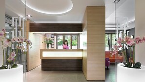 A modern reception area with a wooden reception desk, large potted orchids, and a view of the outdoors through glass doors. - Liv'Inn Aparthotel (Kraków)