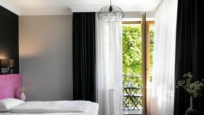 A hotel room with a bed, a desk, a chair, a window with curtains, and a view of greenery outside. - Liv'Inn Aparthotel (Kraków)
