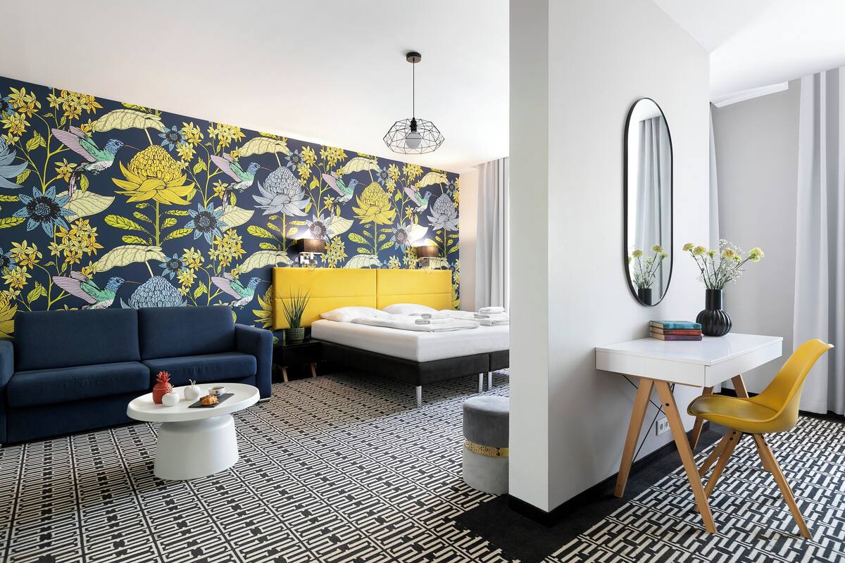 Et moderne hotelværelse med et mønstret gulv, en sofa, en seng, et skrivebord og et spejl.