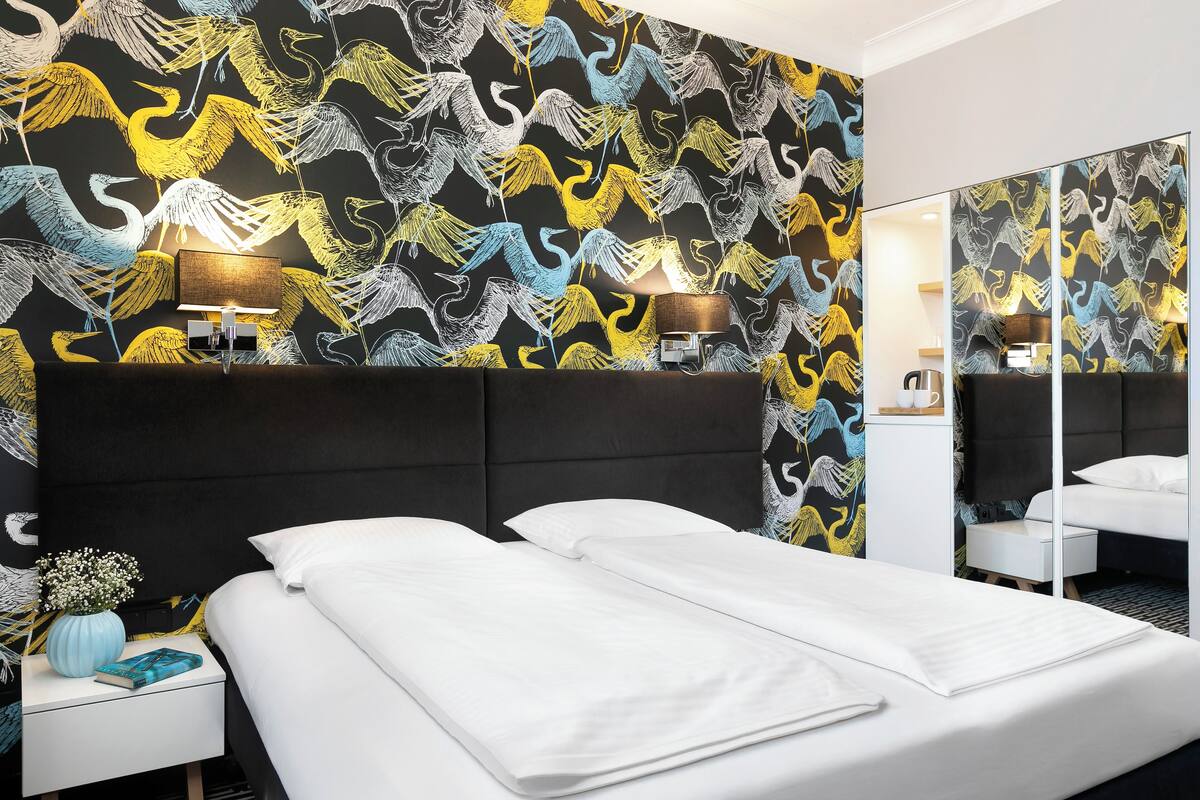 Et hotelværelse med en stor seng, et natbord med en lampe, et spejl og en væg med tapet.