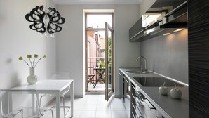 A modern kitchen with a white table and chairs, a vase with flowers, and a view through an open door to an outdoor area. - Liv'Inn Aparthotel (Kraków)