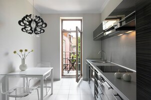 Una cocina moderna con una mesa y sillas blancas, un florero con flores y vistas a un espacio exterior por una puerta abierta.