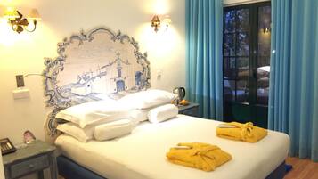 Habitación de hotel con cama, mesita de noche, lámpara, un cuadro y vistas al exterior.