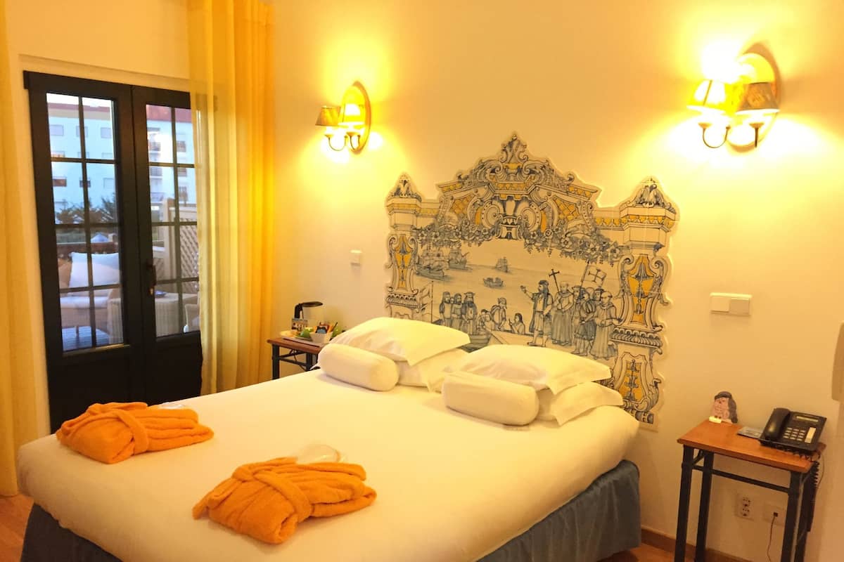 A hotel room with a large bed, two bedside tables, a nightstand, and a view through a window.