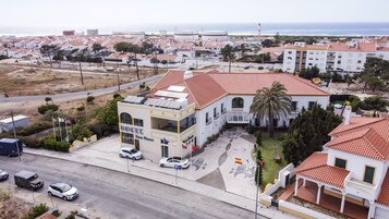 Un pueblo costero con un edificio destacado que tiene paneles solares en el techo, un estacionamiento y vista al mar.