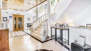 Un vestíbulo amplio con techo de madera, una escalera monumental y una recepción.