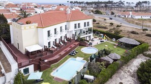 A large building with a swimming pool, outdoor seating, and a fenced garden area. - Hotel Dom Vasco (Sines)