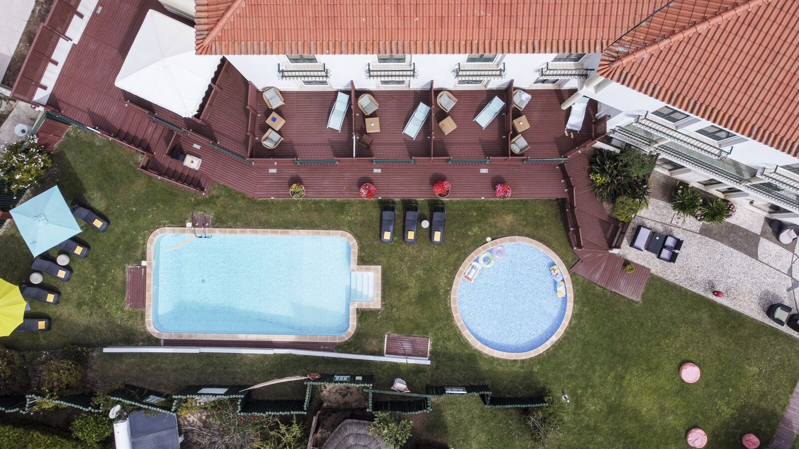 A rooftop pool area with two pools, sun loungers, and a covered seating area.