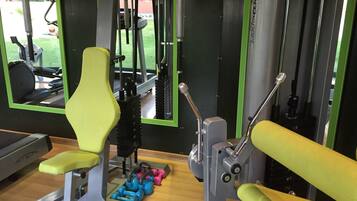 Een fitnessruimte met trainingsapparatuur, waaronder een bank, gewichten en een krachttrainingapparaat.