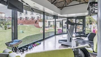 Un gimnasio moderno con amplios ventanales, equipamiento de ejercicio y vistas a una zona residencial.