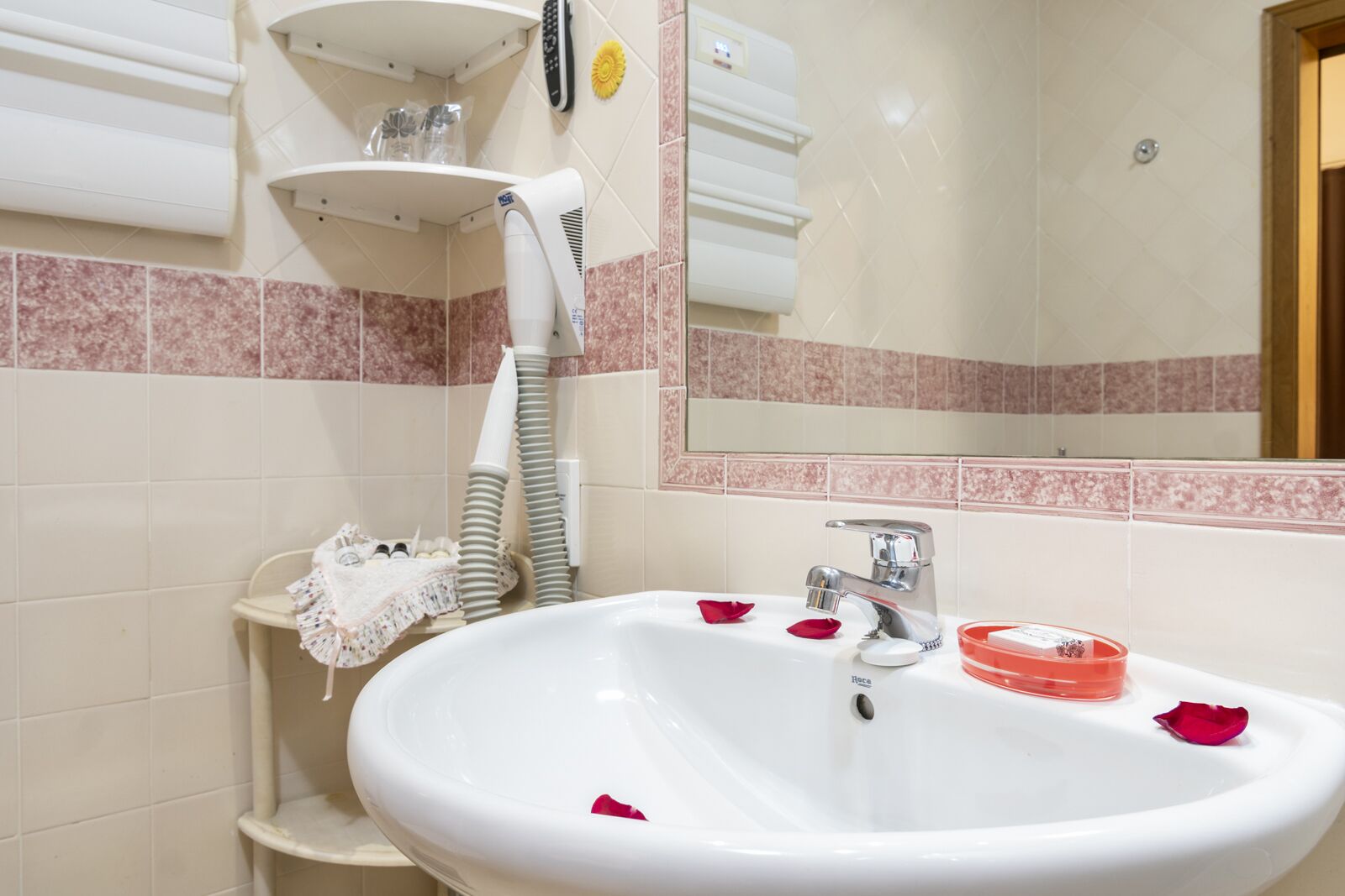 Un baño con un lavamanos blanco, un espejo y un perchero para toallas.