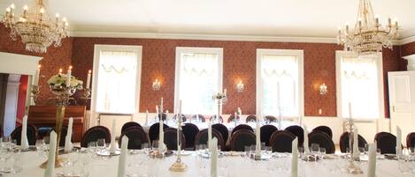 A formal dining room with a long table set for a meal, chandeliers, and large windows with curtains.