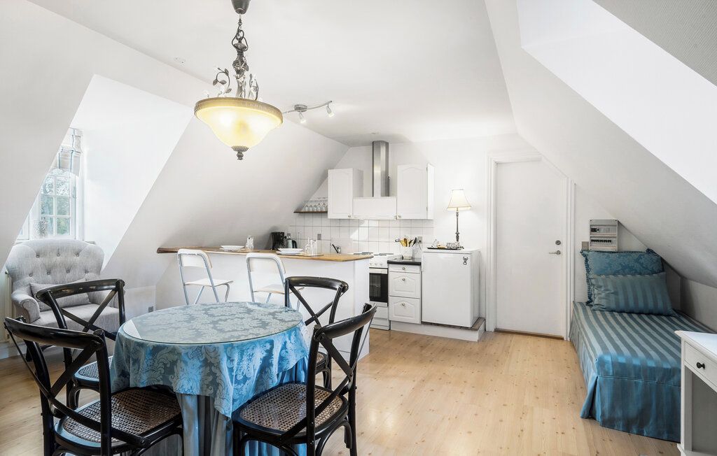 A compact kitchen with white cabinets, a dining table with chairs, and a small sleeping area with a bed.