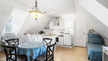 A compact kitchen with white cabinets, a dining table with chairs, and a small sleeping area with a bed.