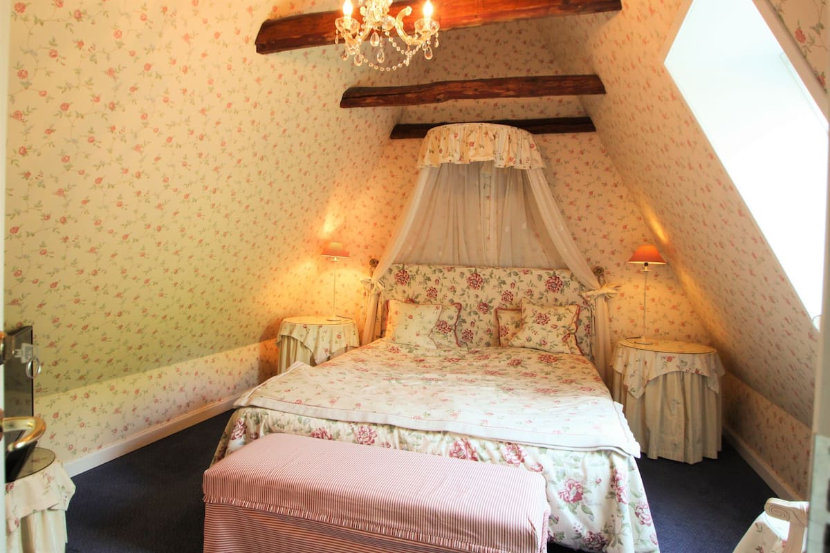 A bedroom with a floral-patterned bed, a canopy, two bedside tables, and a chandelier.