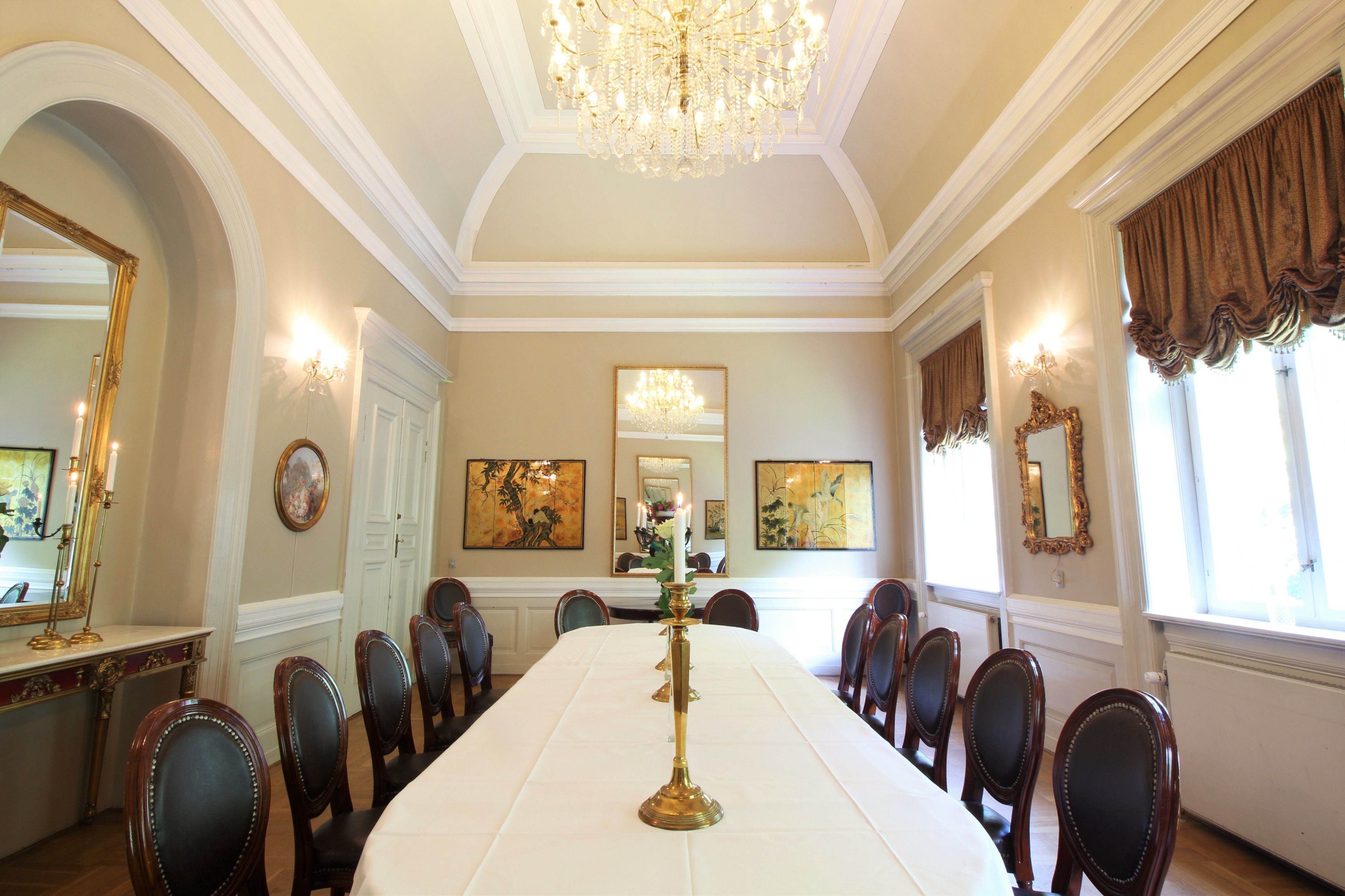 Een chique eetzaal met een lange tafel, stoelen, kroonluchters en kunstwerken aan de wanden.