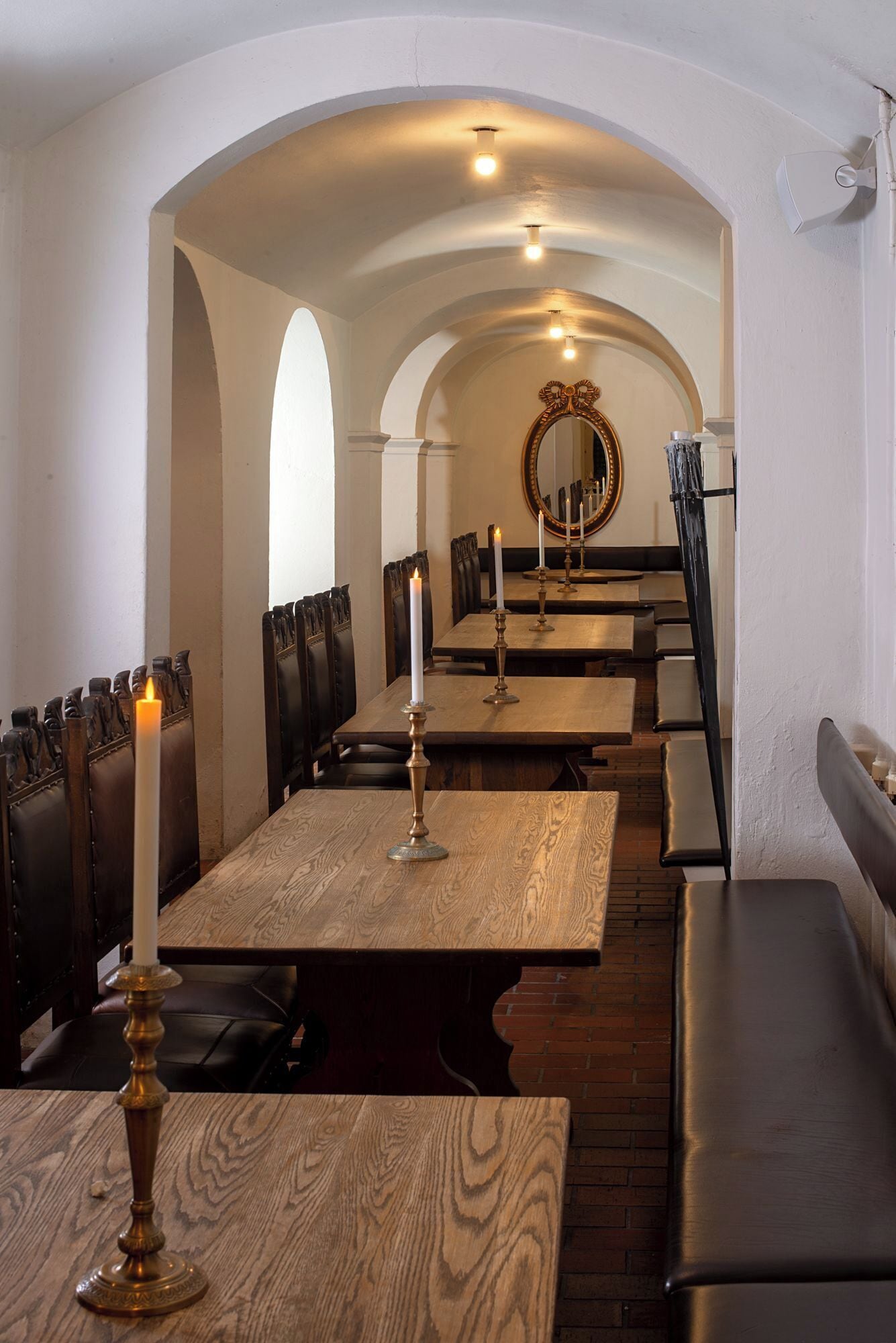 A restaurant with wooden tables and benches, candles, and a mirror on the wall.