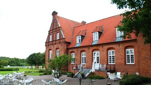 A red brick building with a large patio area featuring outdoor seating. - Sophiendal Slotshotel (Skanderborg)