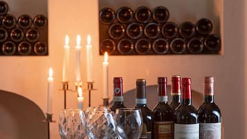 Et træfad med vinflasker og glas på et bord, stearinlys og en væg med vinflasker i baggrunden.