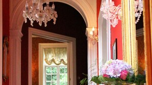 A grand staircase with ornate railings, a chandelier, and a mirror reflecting the room's decor. - Sophiendal Slotshotel (Skanderborg)