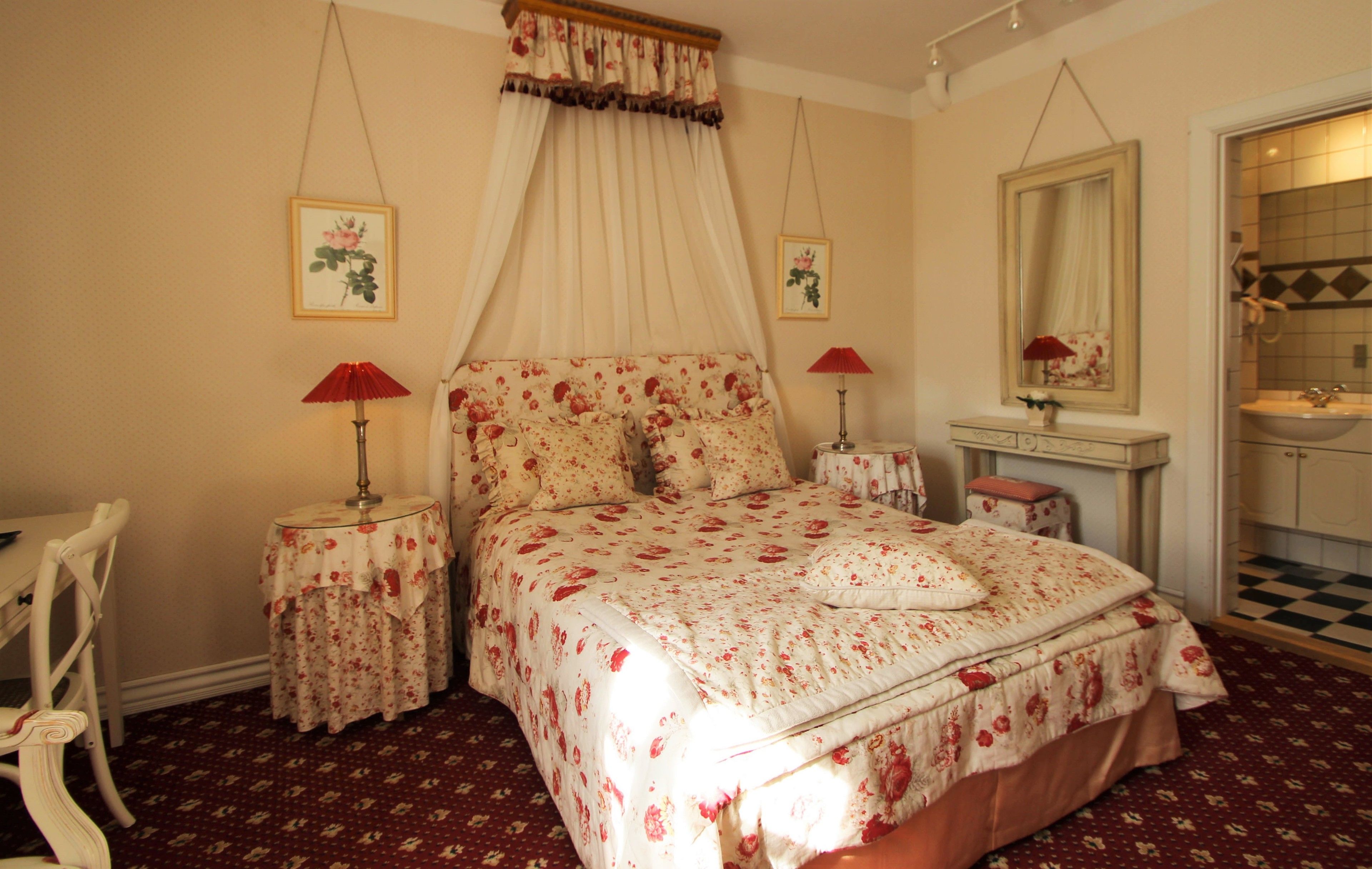 A bedroom with a canopy bed, two bedside tables with lamps, a chair, a dresser, and a mirror.