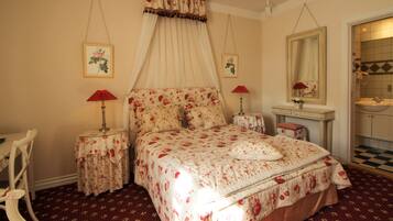 A bedroom with a canopy bed, two bedside tables with lamps, a chair, a dresser, and a mirror.