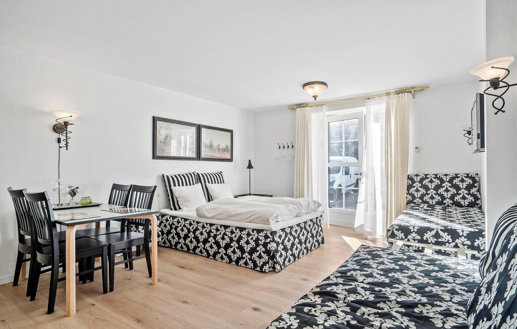 A room with a bed, a sofa, a dining table with chairs, and a window with curtains.