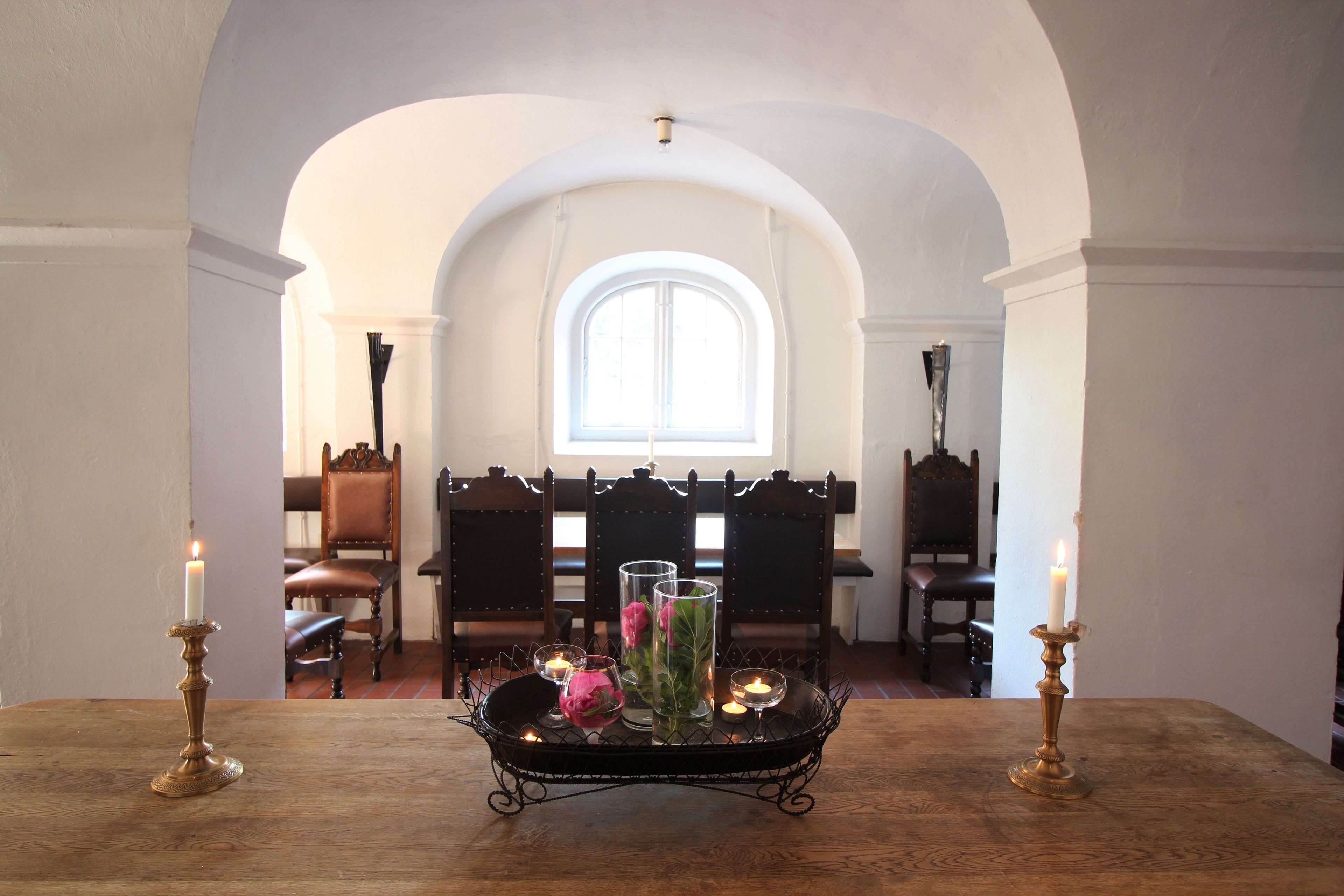 A dining table with candles and a tray of flowers in a room with arched ceilings and wooden chairs.