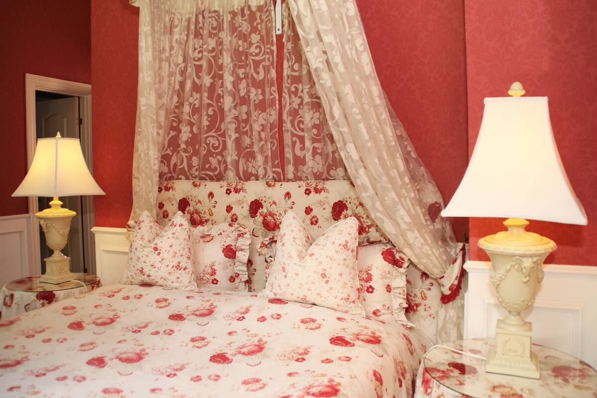 A bed with floral bedding, a canopy, and two bedside lamps.