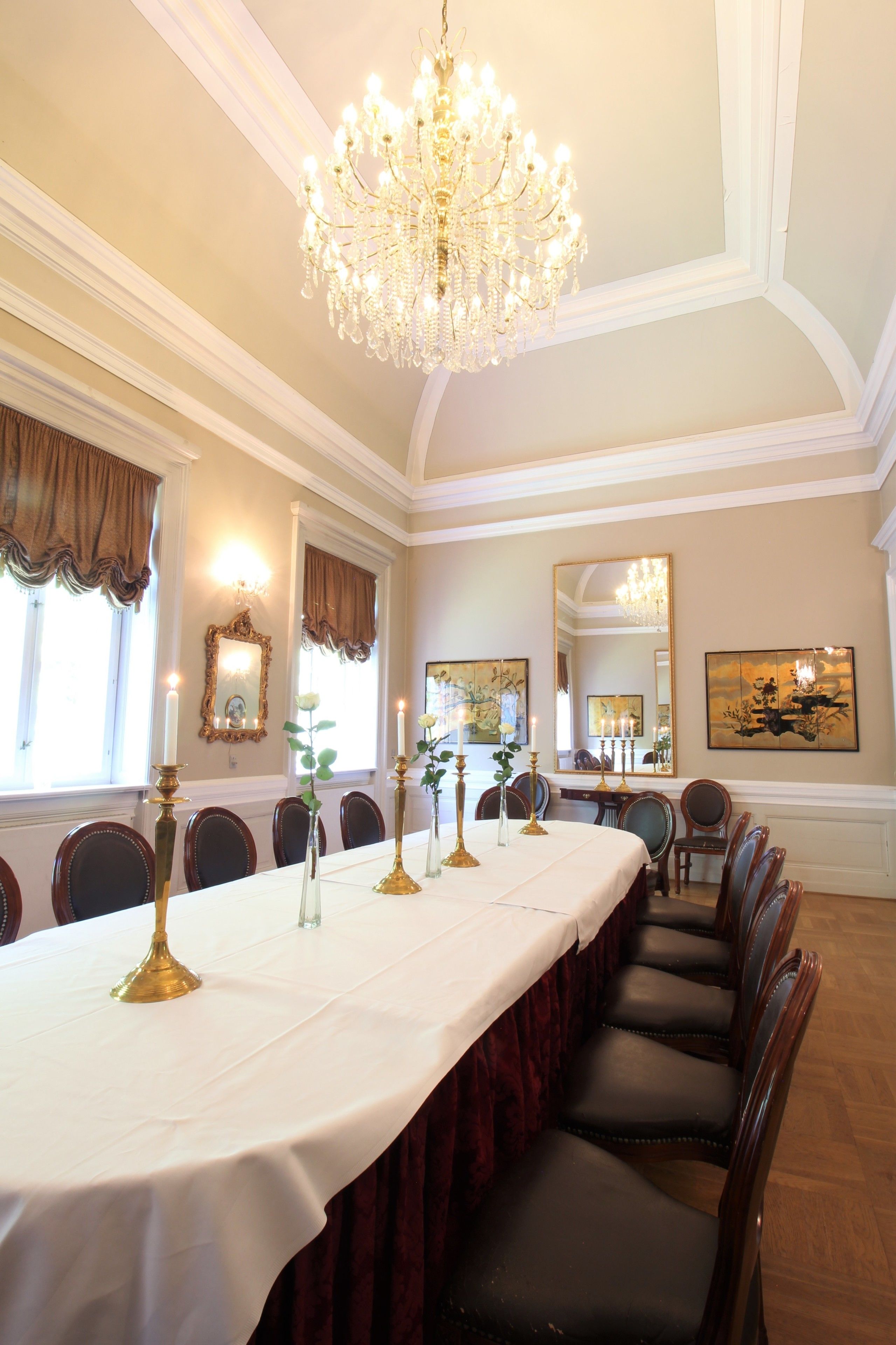 Un comedor formal con una larga mesa dispuesta para un banquete, candelabros y obras de arte enmarcadas en las paredes.
