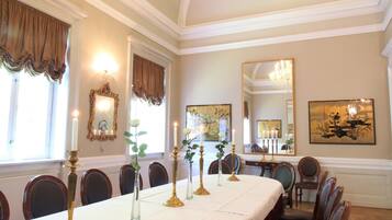 A formal dining room with a long table set for a banquet, chandeliers, and framed artwork on the walls.