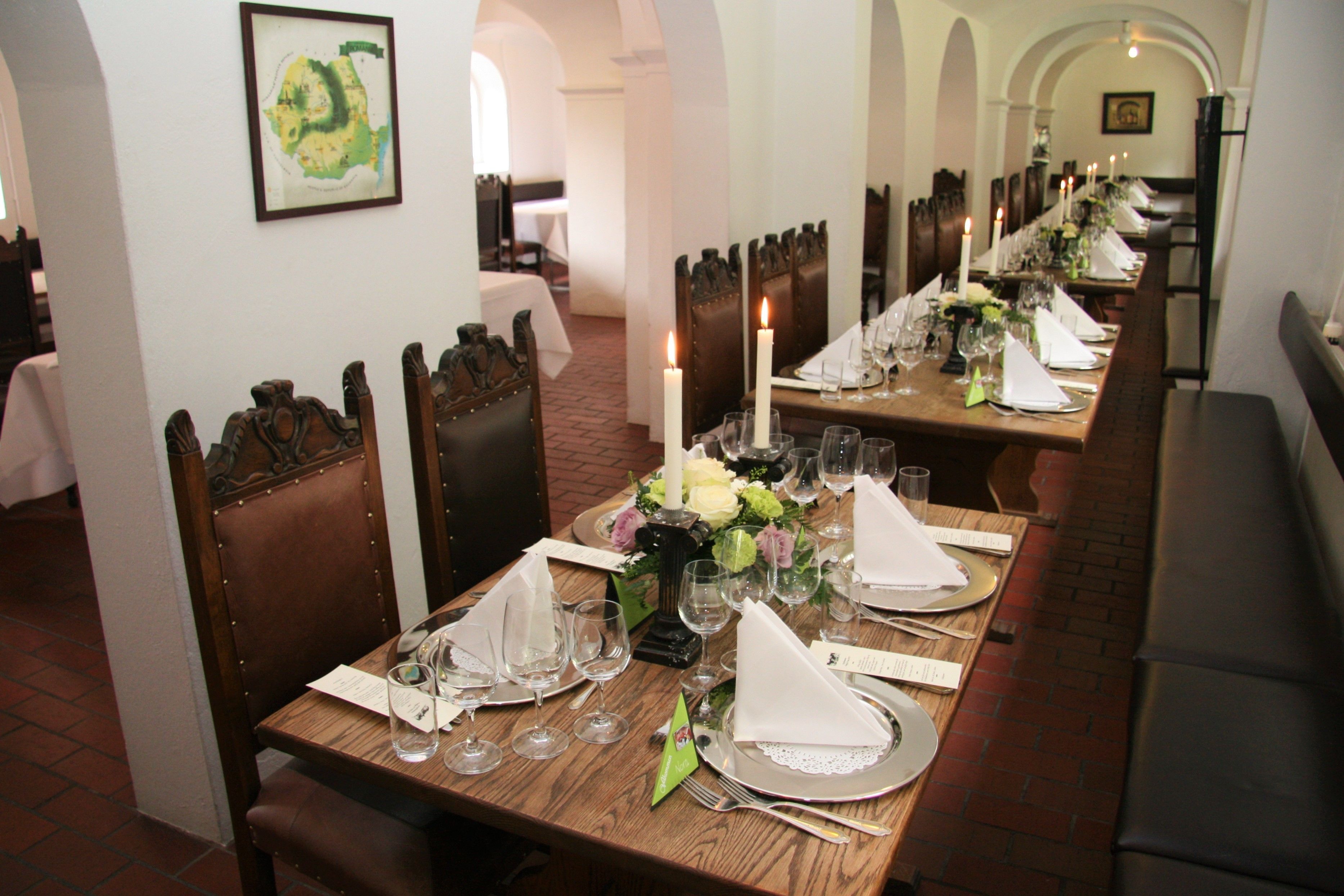 Uma longa mesa de jantar posta com velas, pratos e copos, ladeada por cadeiras de madeira.