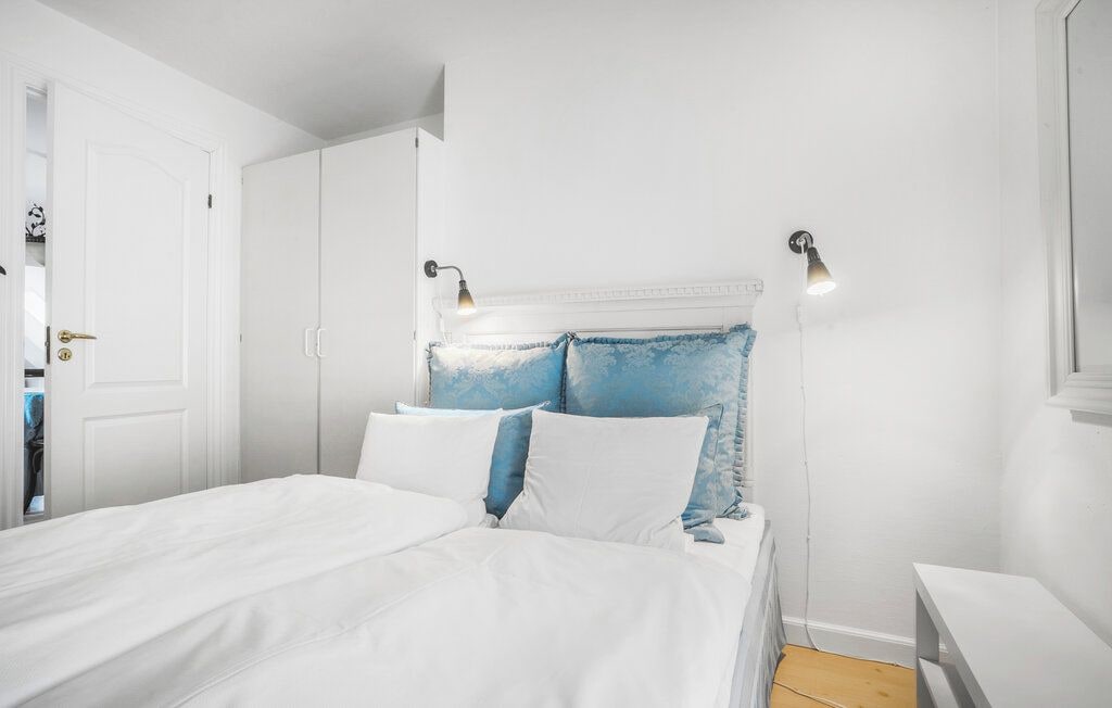 Un dormitorio con cama, paredes blancas, una puerta y dos luces fijadas a la pared.