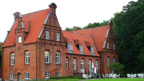 A large brick building with a steeply pitched roof, multiple windows, and a well-maintained lawn with outdoor seating. - Sophiendal Slotshotel (Skanderborg)